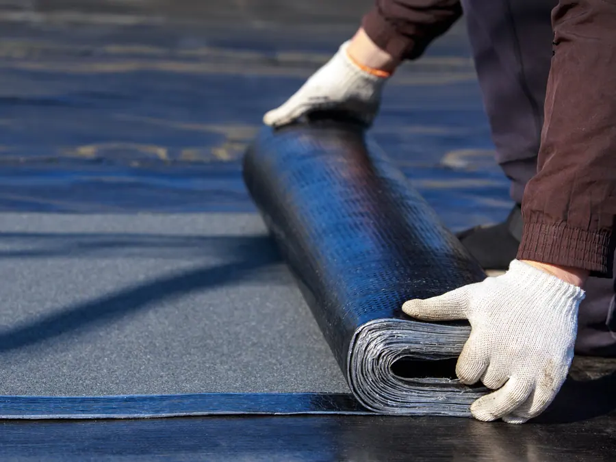 Roll of bitumen roofing felt being laid out on a flat roof