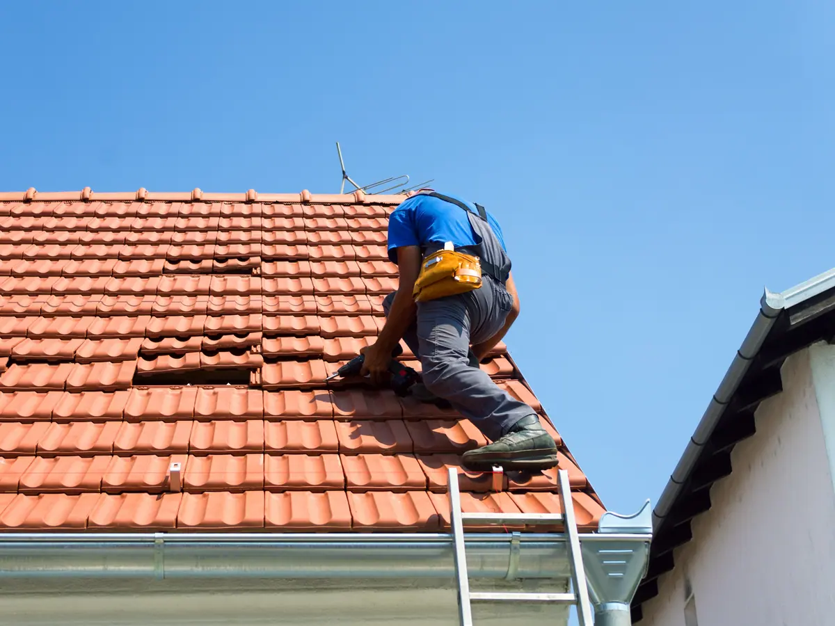Roofer working on a clay tile roof above the gutter, with a ladder at the eaves